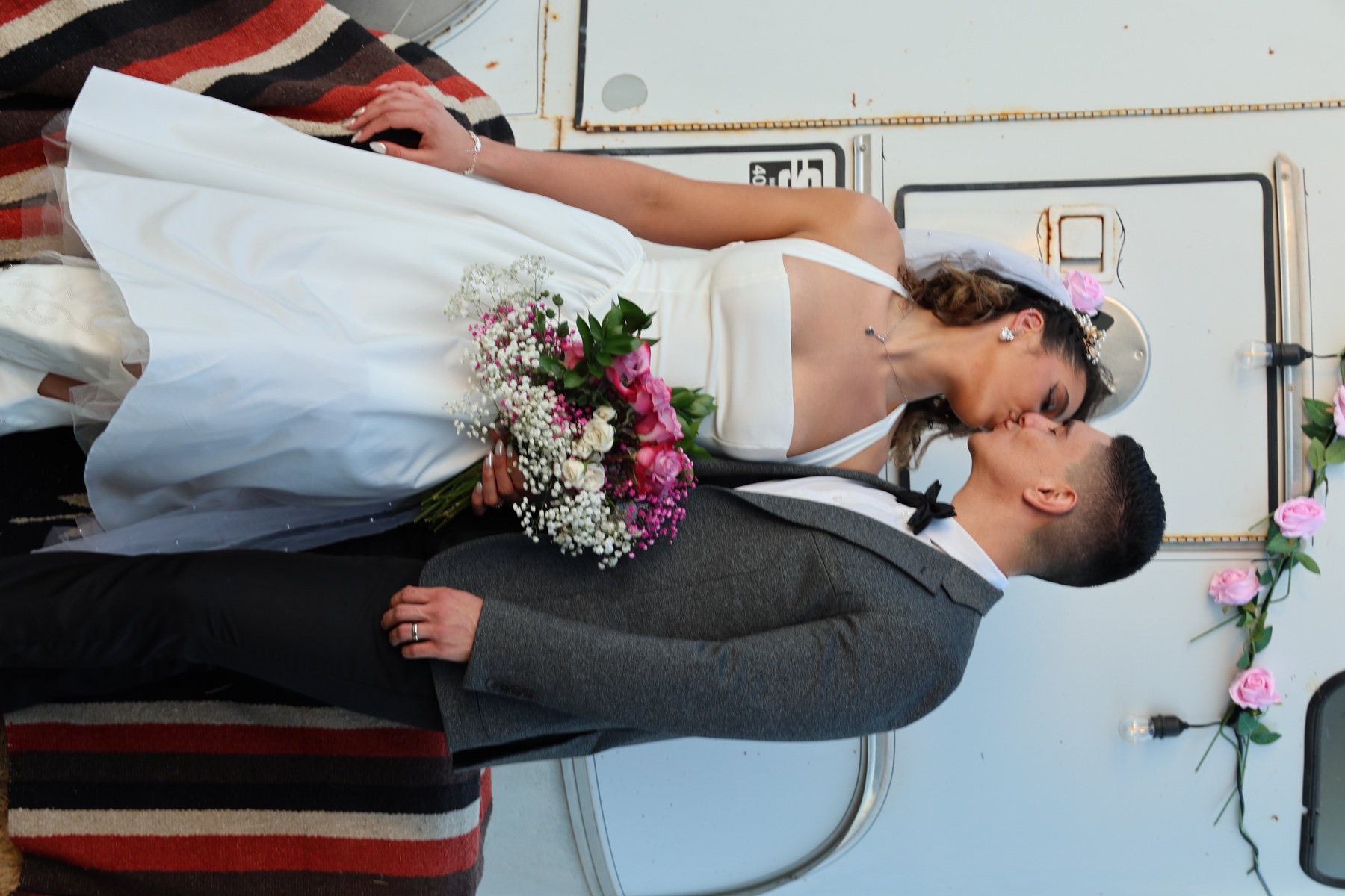Newlyweds sharing a kiss beside a vintage horse trailer