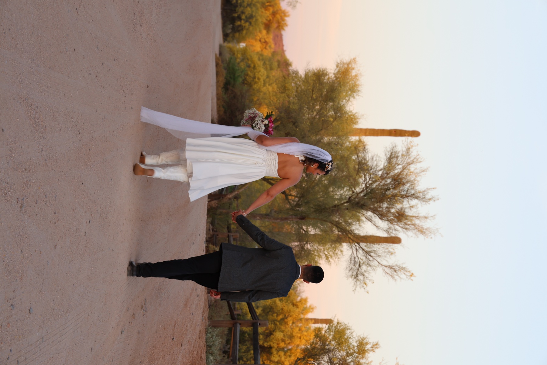 Newlyweds walking hand in hand along a desert road at golden hour